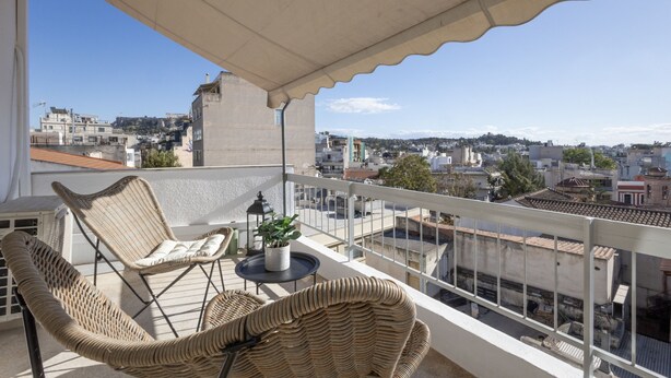 A balcony with wicker furniture, a potted plant, and a view of a cityscape. - Loft at Historical Center of Athens w Acropolis View (Athens)