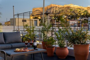 A rooftop terrace with a sofa, table, wine glasses, and a plate of food. - Paradise Suite With Jacuzzi Acropolis View (Athens)