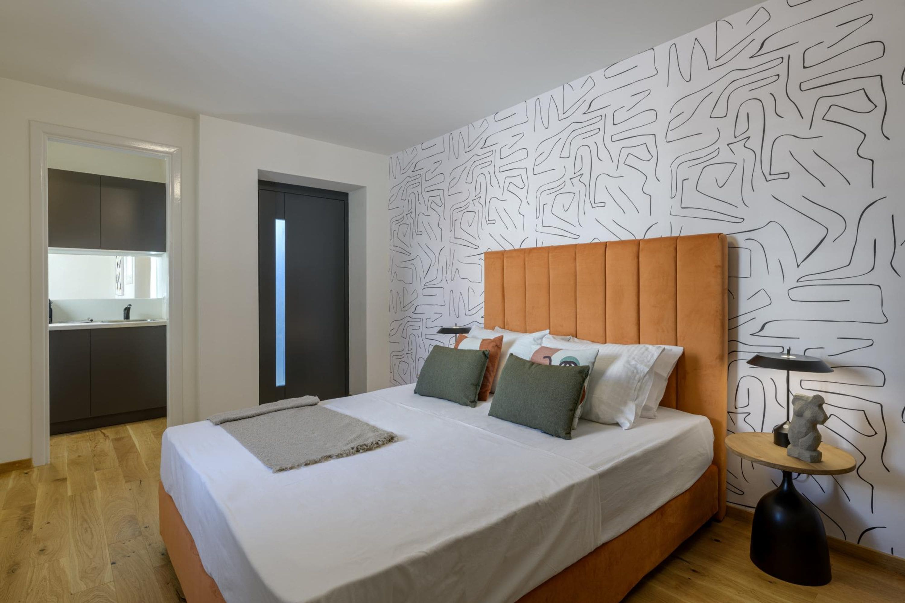 A modern bedroom with a large bed, a wooden headboard, and a patterned wall.