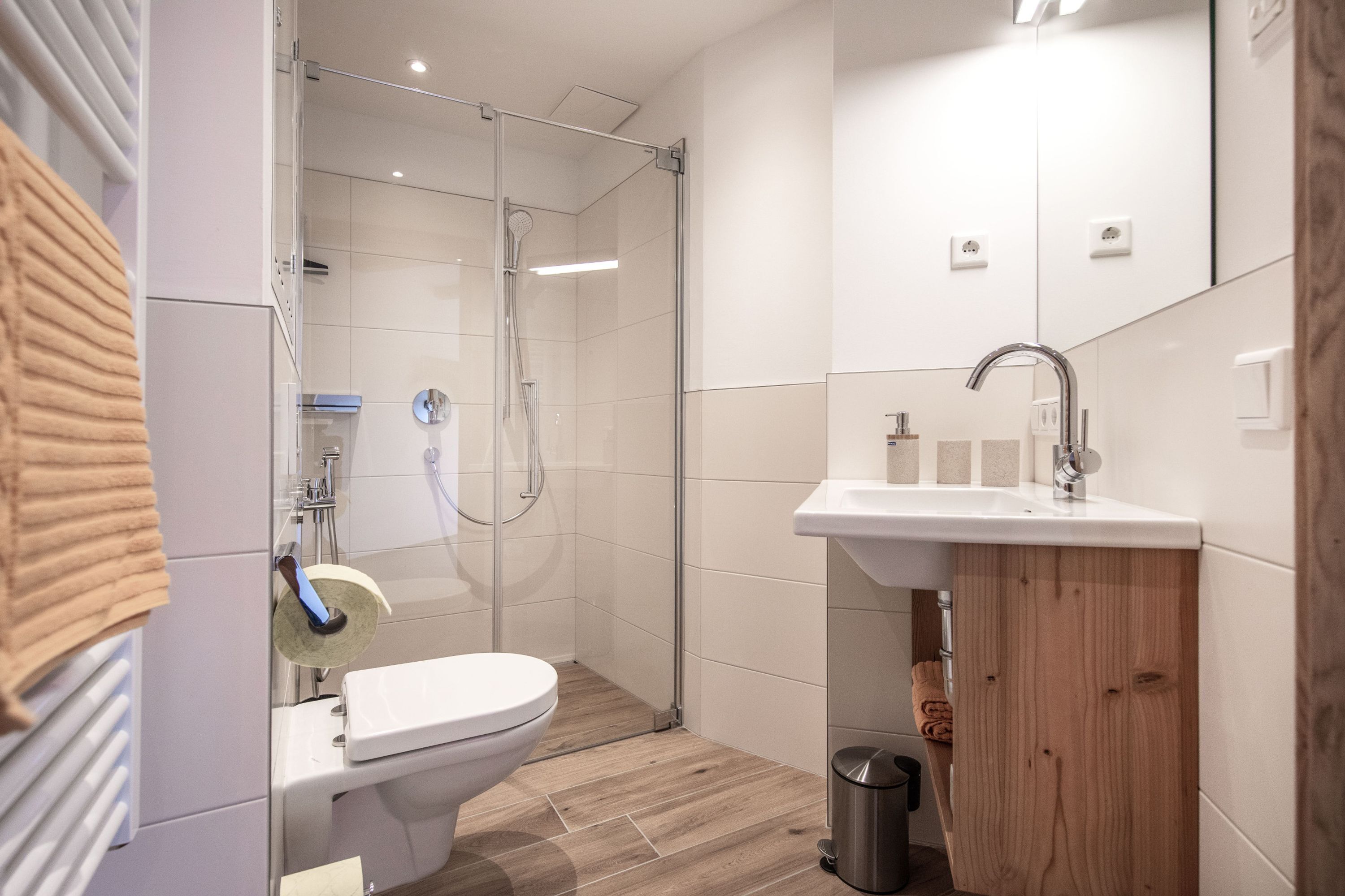 A modern bathroom with a shower, toilet, sink, and wooden cabinet.