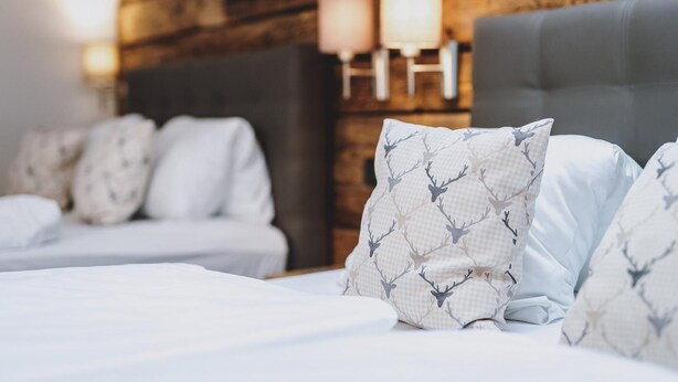 Ein Hotelzimmer mit einer Holzwand, einem grau gepolsterten Kopfteil und weißer Bettwäsche.
