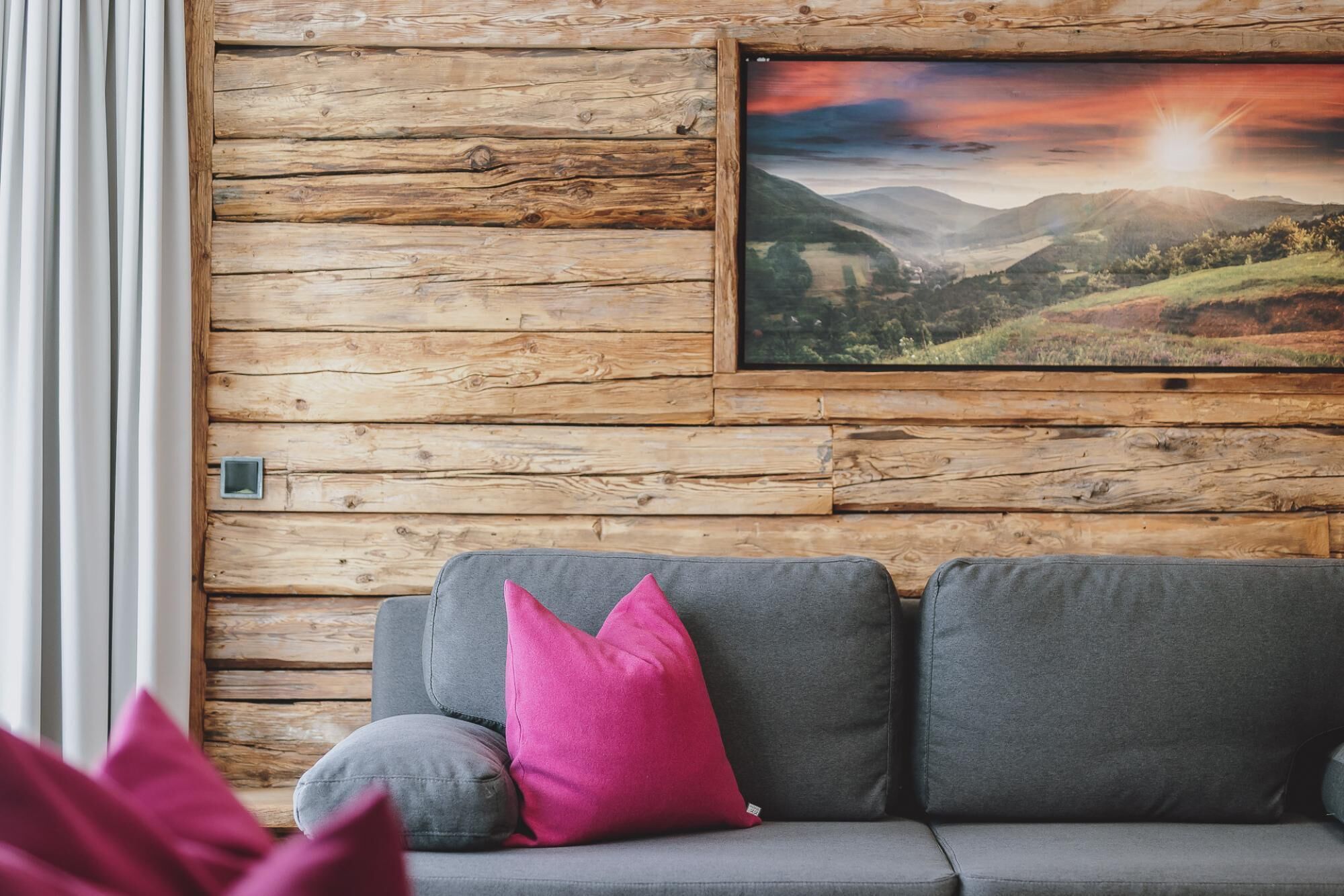 Une pièce avec un canapé gris, un mur en bois et un tableau représentant un paysage, encadré.