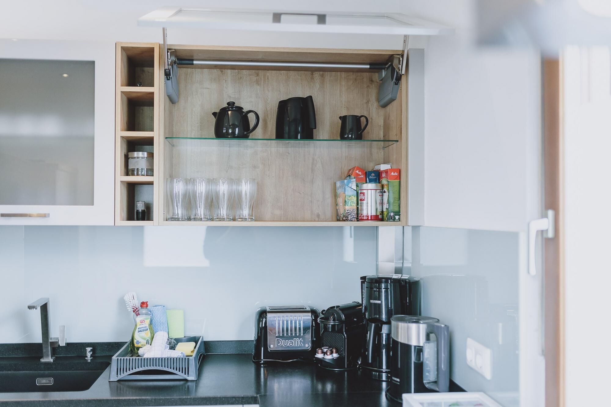 Una cocina con un mueble de madera, una cafetera y un lavabo.