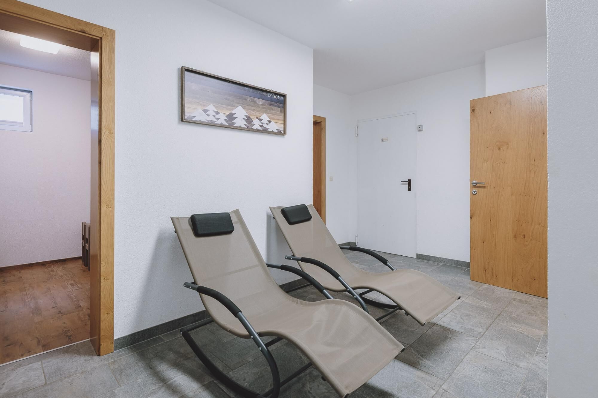 A hallway with two reclining chairs, a wooden door, and a framed picture on the wall.