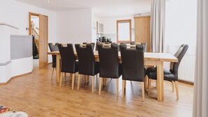 Ein moderner Essbereich mit einem Holztisch und schwarzen Stühlen, im Hintergrund eine Küche und eine Treppe, die zu einer anderen Etage führt.