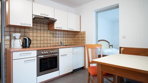 A compact kitchen with white cabinets, a stove, a coffee maker, and a dining area with a table and chairs.