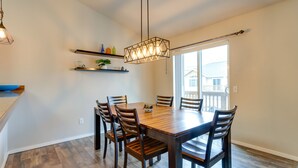 Un'area pranzo con un tavolo e sedie in legno, un lampadario, mensole con oggetti decorativi e vista attraverso un'ampia finestra.