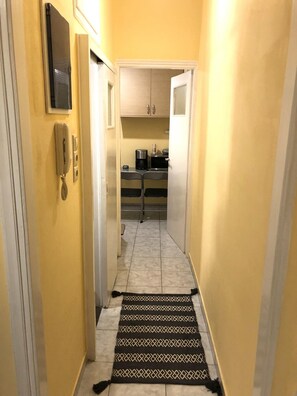 A narrow hallway with a patterned rug, a telephone, and a kitchen area visible through an open door. - Cozy Studio at Kallithea (Kallithea)