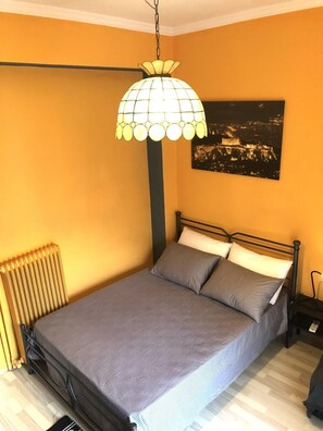 A bedroom with a bed, a radiator, a nightstand, and a wall-mounted lamp. - Cozy Studio at Kallithea (Kallithea)