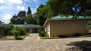 A building with a paved driveway leading to a gated entrance, surrounded by greenery and trees.