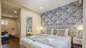 Una habitación de hotel con una cama grande, una mesita de noche, un espejo y un baño a la vista al fondo.