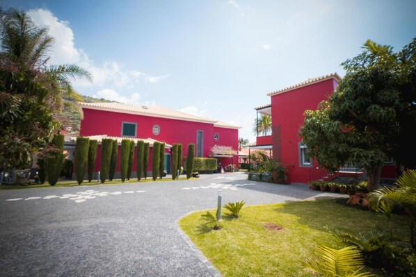 A red building with a paved driveway and well-maintained lawn. - Quinta da Tia Briosa Casa da M e I by Homie (Ponta do Sol)