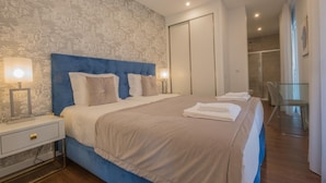 Una habitación de hotel moderna con una cama grande, una mesita de noche, una lámpara y un baño visible a través de una puerta abierta.