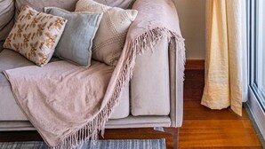 Ett mysigt vardagsrum med en beige soffa, mönstrade kuddar och en väggdekoration i makramé.