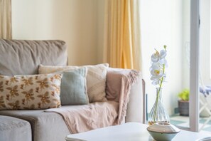 A living room with a sofa, decorative pillows, a vase with white flowers, and a view of the outdoors. - Bellemar Apartment by Homie (Funchal)