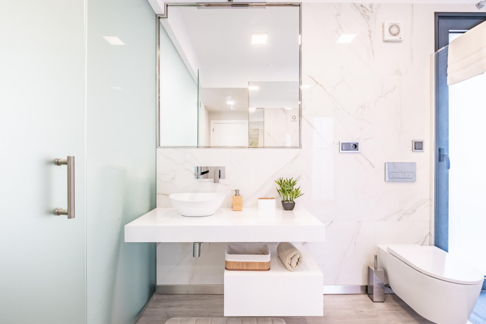 A modern bathroom with a white sink, a large mirror, a towel rack, and a toilet.