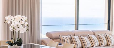 A modern living room with a glass table, beige sofa, and white orchids.