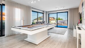 A modern living room with a pool table, large windows, and a view of the outside.