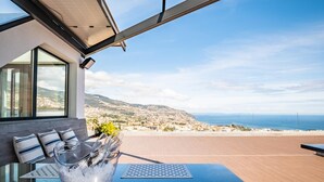 A modern outdoor seating area with a clear view of the sea and hills.