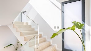 A modern staircase with glass railings and wooden steps, leading to a door with a frosted glass panel.