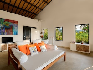 Relax in a spacious bedroom with a large bed, flat-screen TV, and a window offering a view of lush greenery and mountains.
