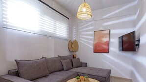 Un salon moderne avec un canapé d’angle gris, une table basse ronde en bois, un téléviseur fixé au mur et un élément décoratif représentant des feuilles.