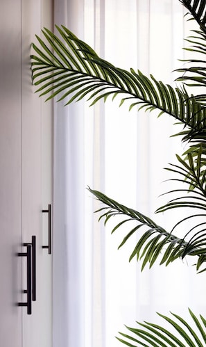 Une pièce avec un meuble blanc et des poignées noires, partiellement dissimulé par une grande plante verte aux longues feuilles.