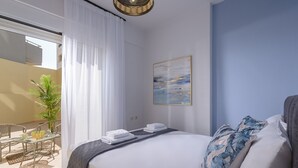 Une chambre d’hôtel avec un lit, un tableau, un balcon avec une table et des chaises, et une plante en pot.