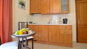 A compact kitchen with wooden cabinets, a white countertop, and a small dining table with fruits. - Katrina Studio 3 With Balcony (Rethymno)