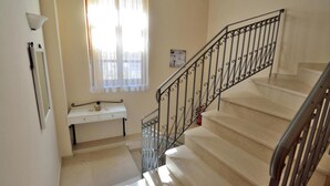A staircase with a metal railing, a white console table, and a window with sheer curtains. - Katrina Studio 3 With Balcony (Rethymno)