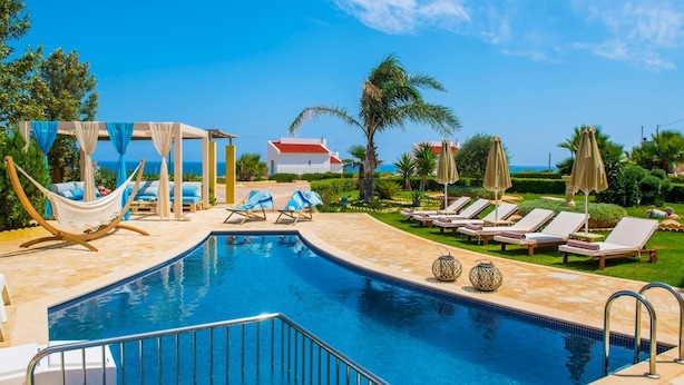 Zona de piscina con vista despejada al mar, sillas de descanso y una hamaca.