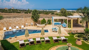 A pool area with lounge chairs, a hammock, and a covered seating area with a view of the sea.
