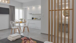 A modern hotel room with a dining area, kitchenette, and a view through a wooden partition. - Myra Mare White Suite by Estia (Heraklion)