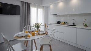 A modern kitchen with white cabinets, a built-in oven, and a sink. There is a dining table with chairs and a vase of flowers. - Myra Mare White Suite by Estia (Heraklion)