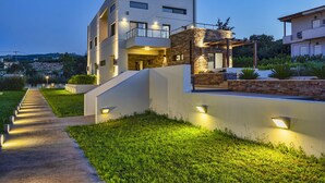 Una moderna casa a più piani con facciata in pietra, un balcone e un vialetto ben illuminato.
