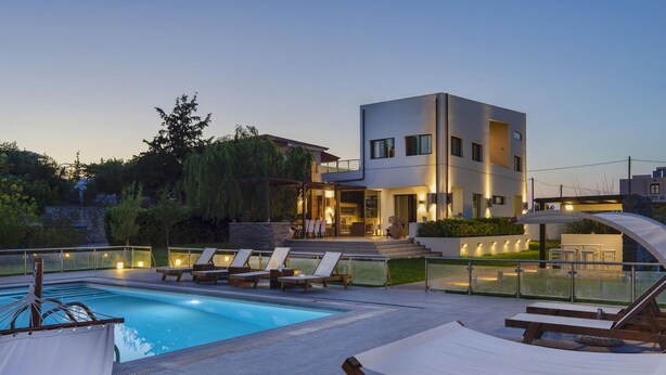 Una casa moderna con piscina, lettini e un'area esterna ben illuminata.