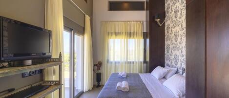 A hotel room with a bed, a television on a wooden shelf, and a window with curtains.