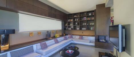 A modern living room with a sectional sofa, a flat-screen TV, a bookshelf, and a coffee table.