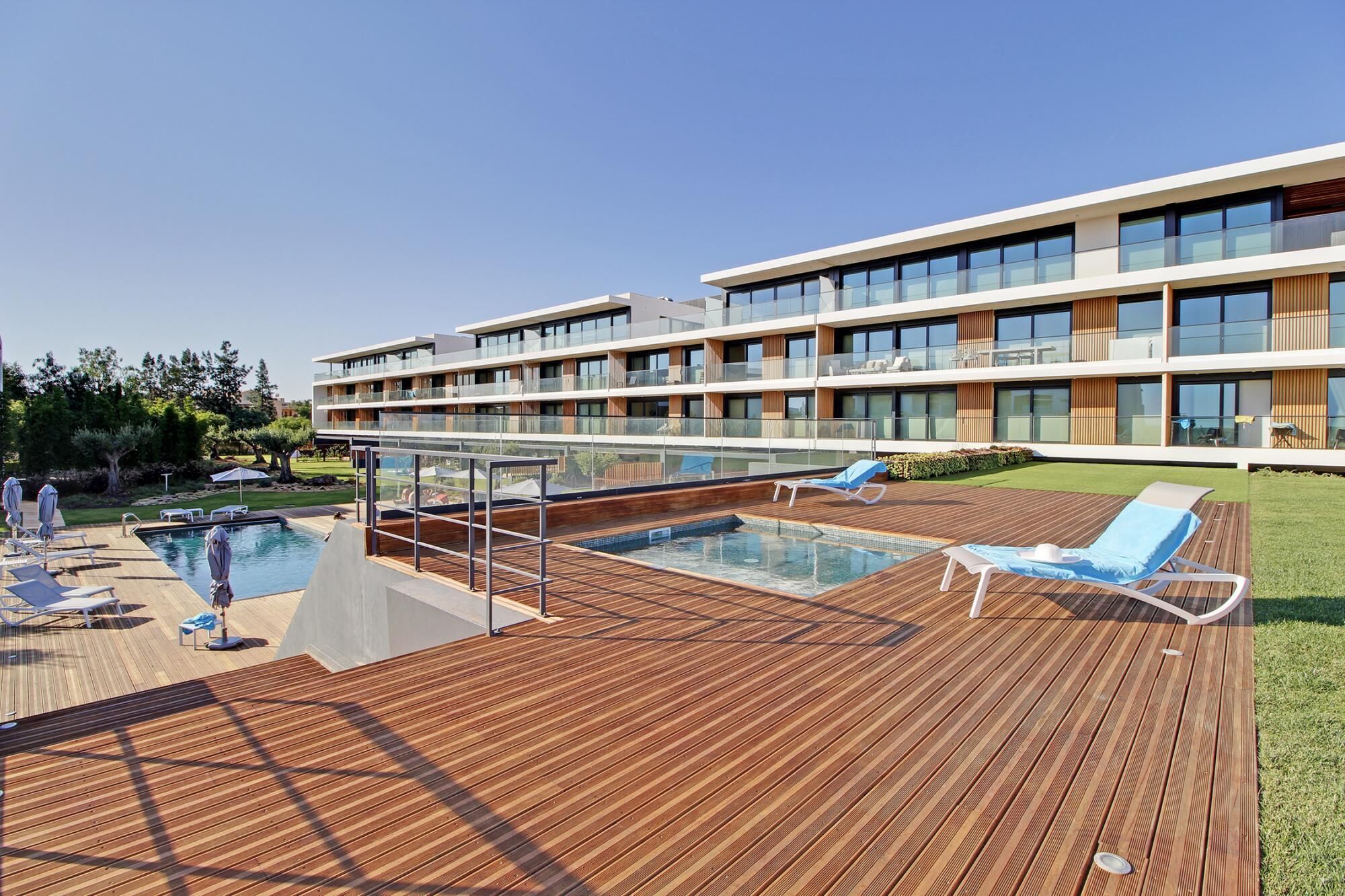 A modern hotel with a rooftop pool area, including lounge chairs and a glass balustrade.