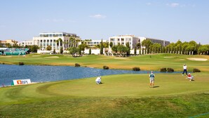 Campo de golfe com um lago, edifícios e céu claro.