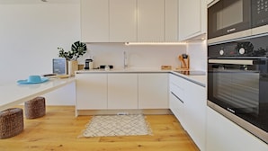Cozinha moderna com armários brancos, forno Bosch e uma pequena ilha com uma planta e um chapéu azul.