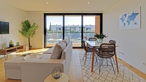 Uma sala de estar moderna com sofá, mesa de jantar, cadeiras e uma grande janela com vista para edifícios.