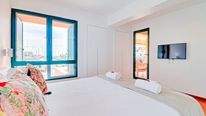 A modern hotel room with a large bed, a TV, a balcony with a view of the city, and a door leading to a balcony. - Garden Marina in Vilamoura (Loulé)