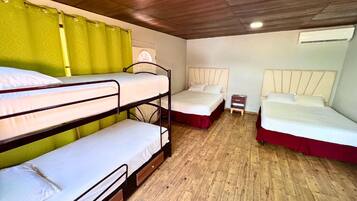 Ein Schlafsaalzimmer mit Etagenbetten, einem Nachttisch, einer Lampe und einer Klimaanlage.