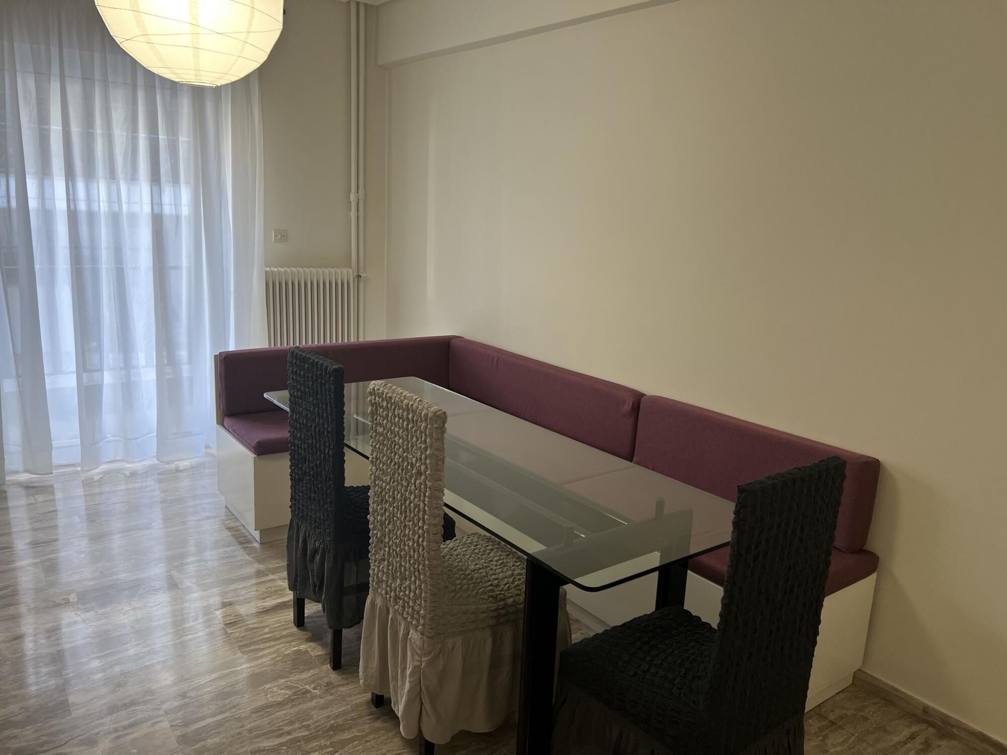A dining area with a glass table, cushioned benches, and a radiator.