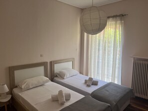 A hotel room with two single beds, a bedside table with a lamp, a large window with sheer curtains, and a radiator. - Retro at Pagrati in Athens (Athens)