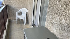A small balcony with a white plastic chair, a table, and a door.