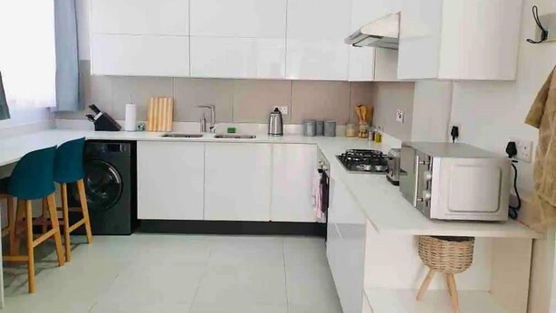 Una cocina moderna con armarios blancos, un fregadero, una estufa y un microondas. Hay taburetes de madera y una cesta en la encimera.