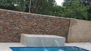 A rectangular swimming pool with a stone wall and a water feature in the center. - Posh 3 Bed Guesthouse in Hillside With Pool - 2039 (Bulawayo)