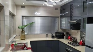 A modern kitchen with a central island, built-in appliances, and a large window with blinds. - Posh 3 Bed Guesthouse in Hillside With Pool - 2039 (Bulawayo)